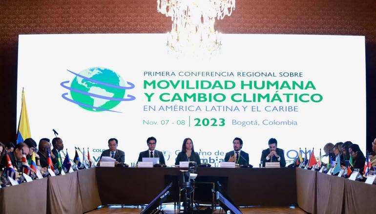 La secretaria de Ambiente, Carolina Urrutia, se encuentra sentada junto a delegados de diferentes países, en una conferencia sobre movilidad humana por cambio climático